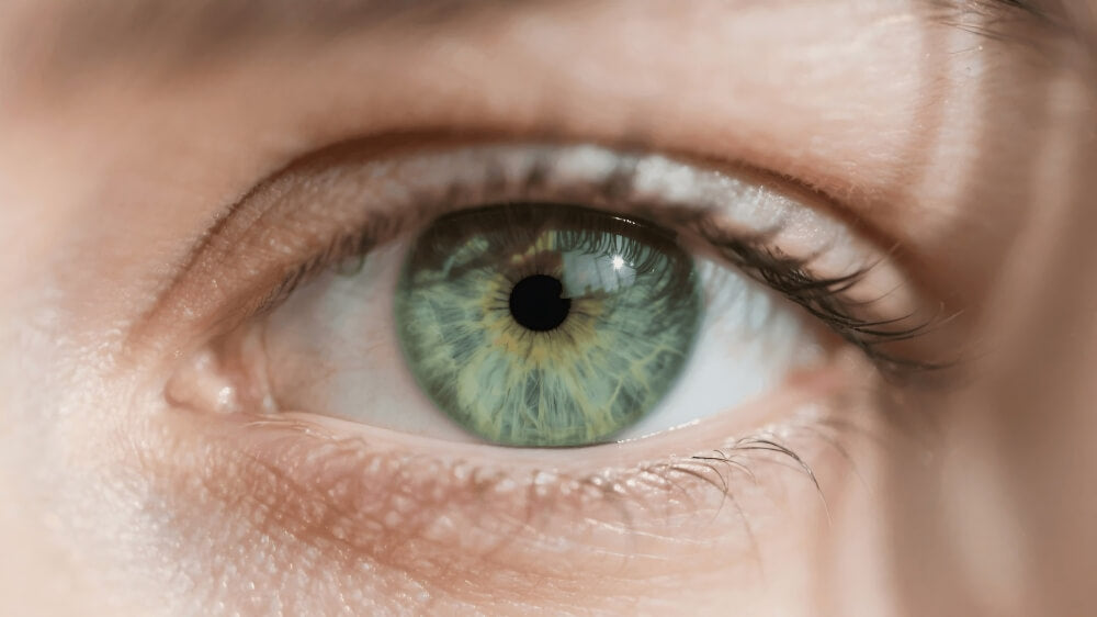 Close-up of a light green eye with intricate iris details and long eyelashes.