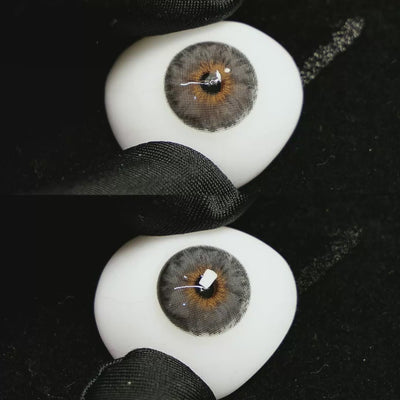 A simulated brown prosthetic eye showing the visual transformation effect of wearing Mermaid Grey colored contact lenses against a black background.