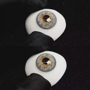 A simulated brown prosthetic eye showing the visual transformation effect of wearing Vegas Grey colored contact lenses against a black background.