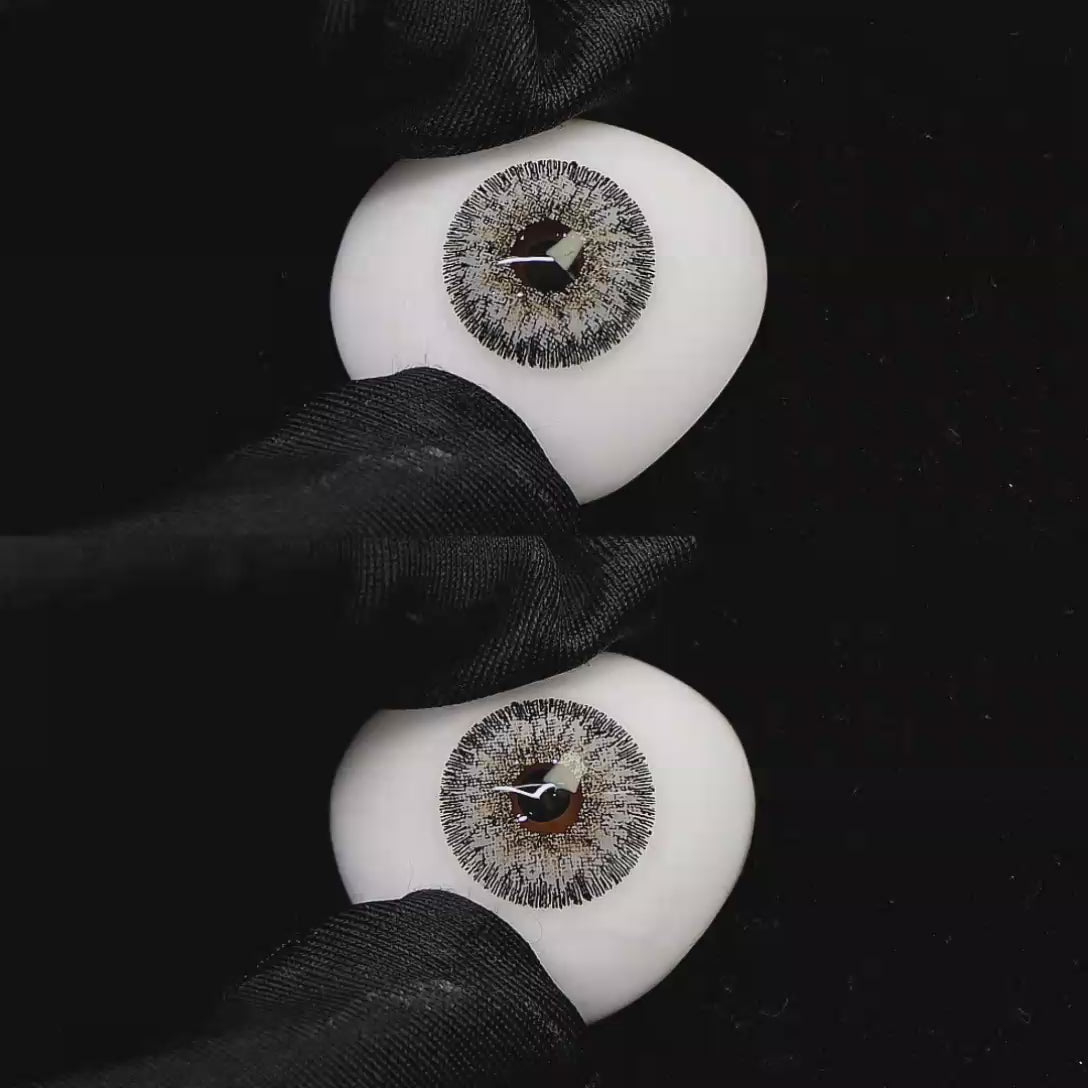A simulated brown prosthetic eye showing the visual transformation effect of wearing Wooeye Galaxy Gray I colored contact lenses against a black background.